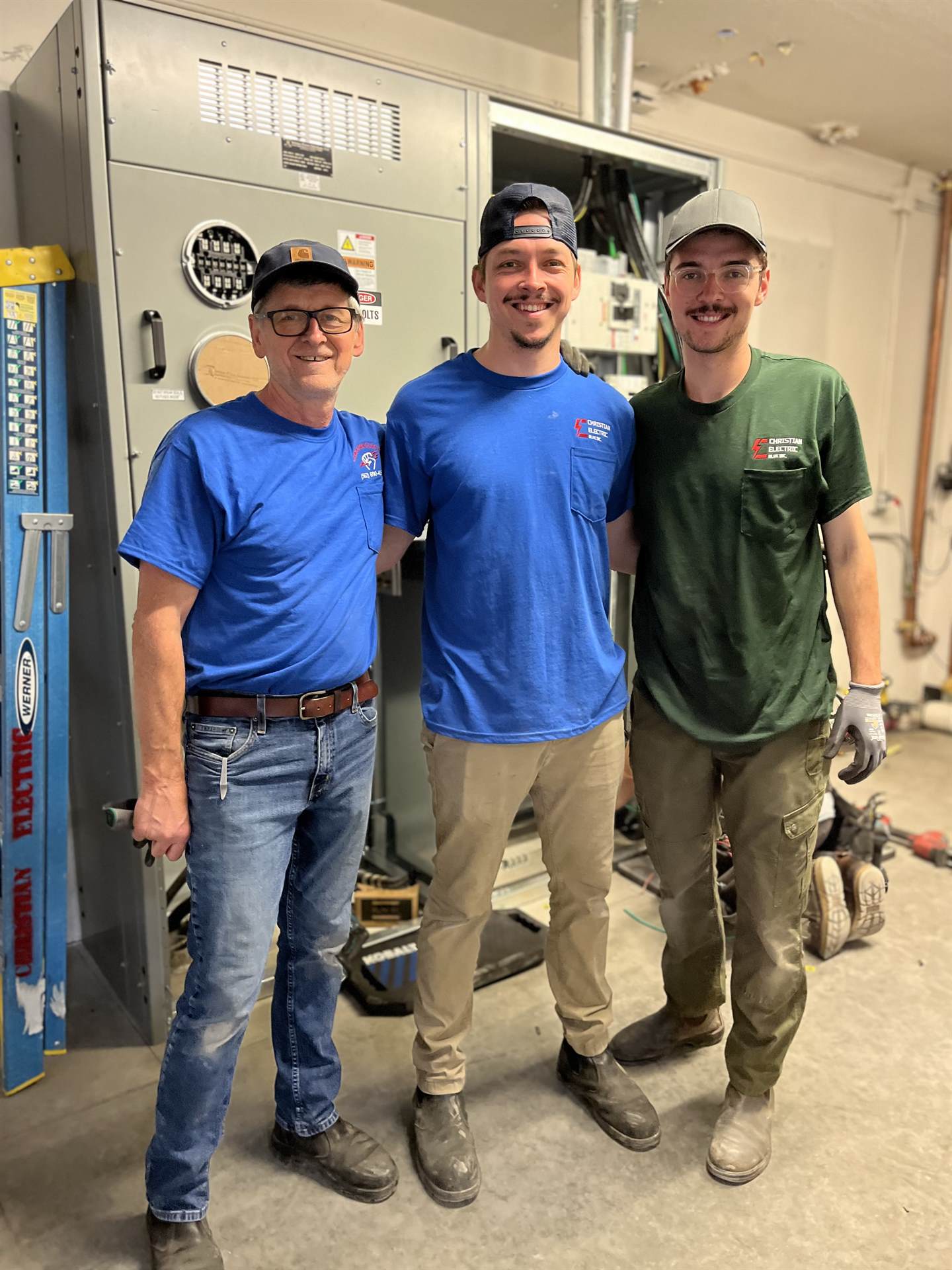 Three Christian Electric Blue electricians standing together in front of a switchgear installation